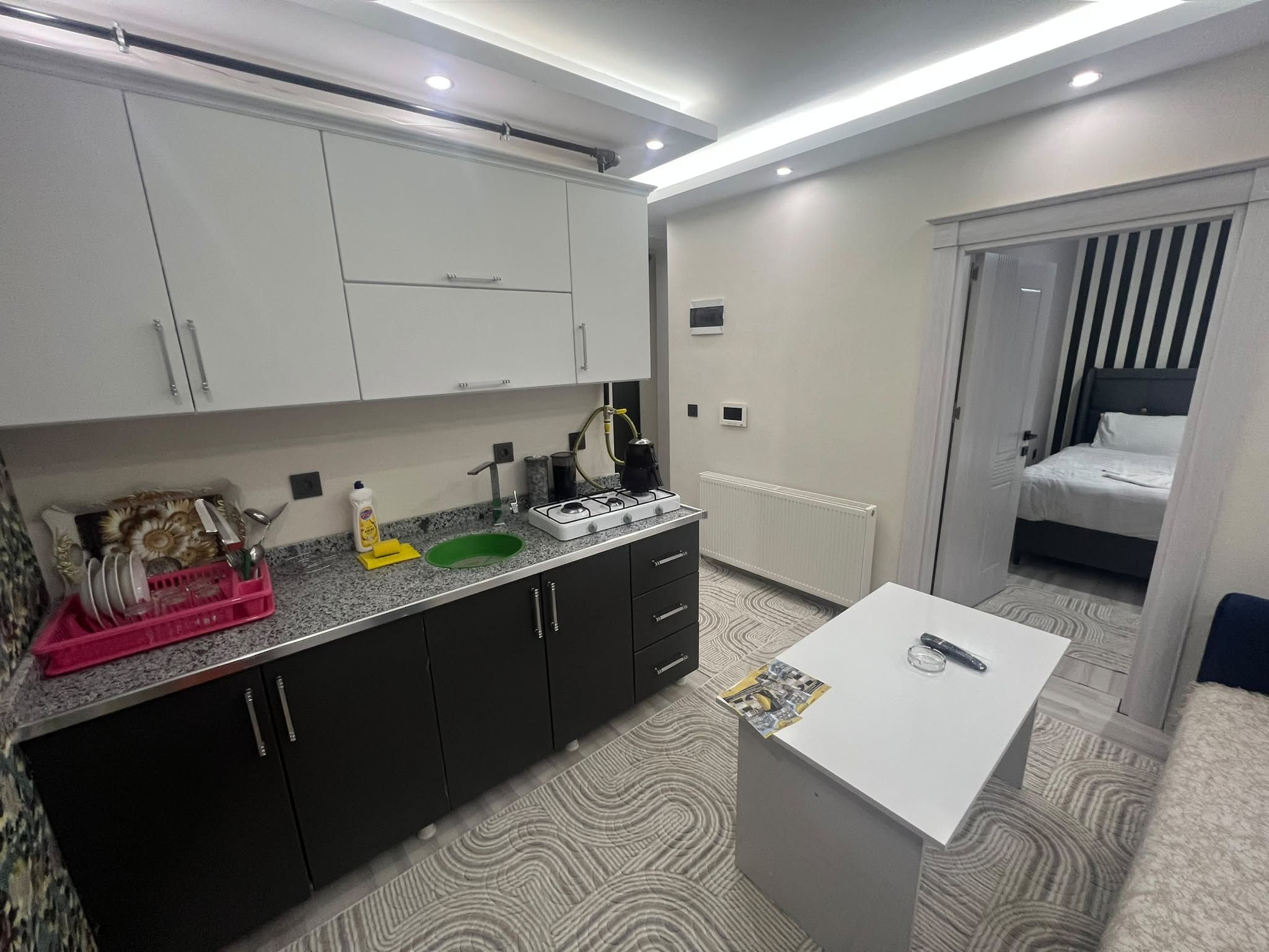 Una cocina moderna con una isla central, una zona de comedor con una mesa, y un dormitorio con una cama.