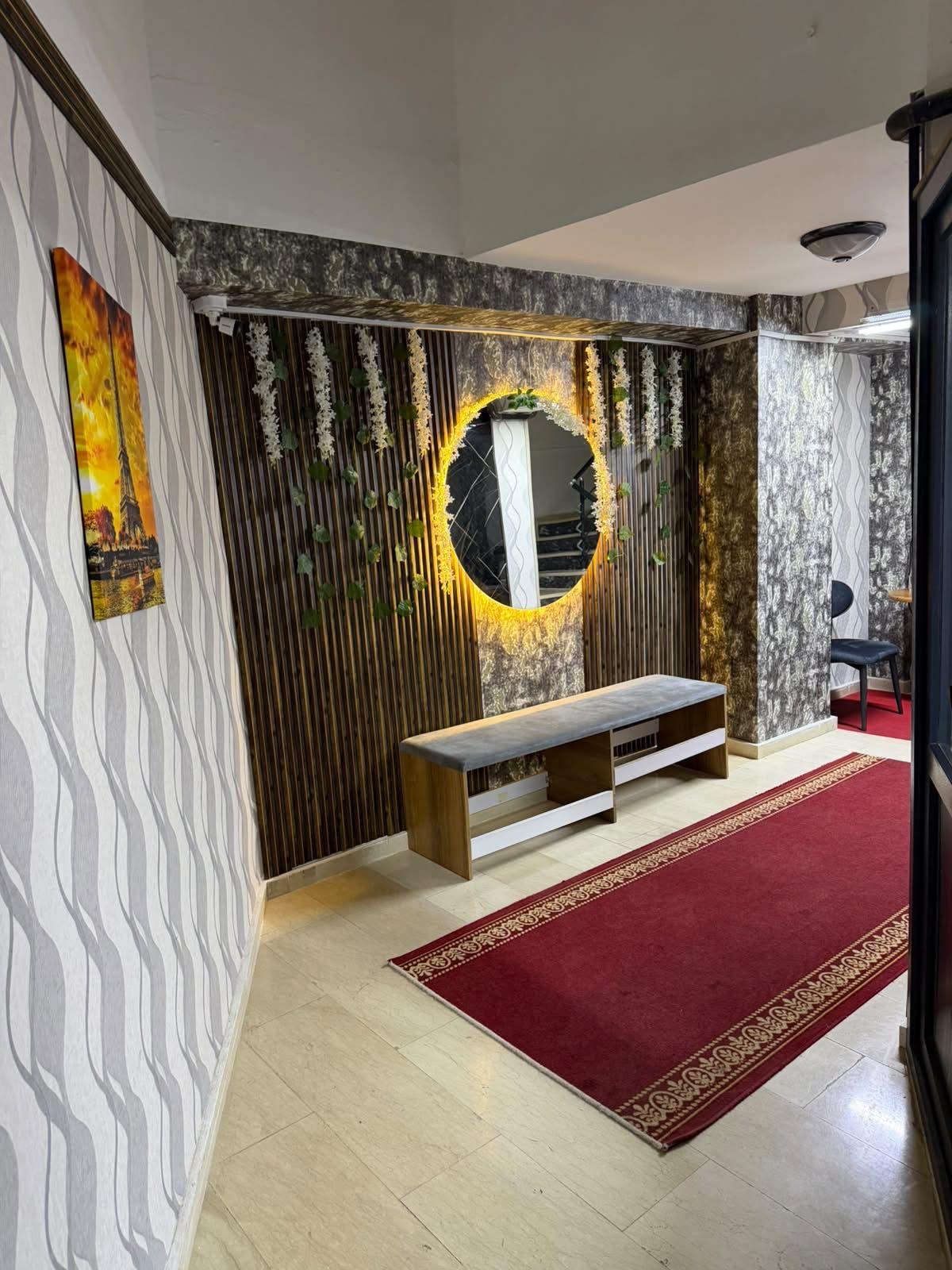 Une pièce avec un tapis rouge, un banc, un miroir doté d’un cadre décoratif et des murs à motifs.