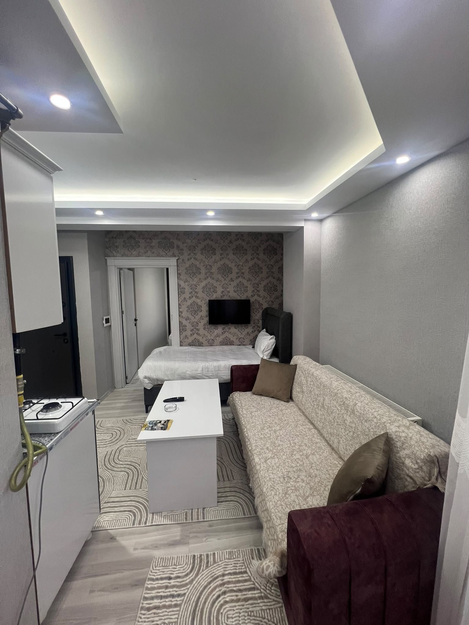 Een moderne hotelkamer met een bed, een slaapbank, een televisie en een kleine kitchenette.