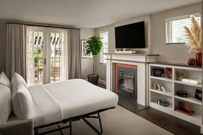Ein modernes Schlafzimmer mit einem großen Bett, einem Kamin, einem Fernseher und Blick ins Freie.