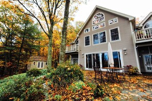 A two-story building with a balcony, a covered patio with outdoor seating, and a surrounding wooded area. - Sacred Dream Entire Property-Hot Tub Copake Lake (Craryville)