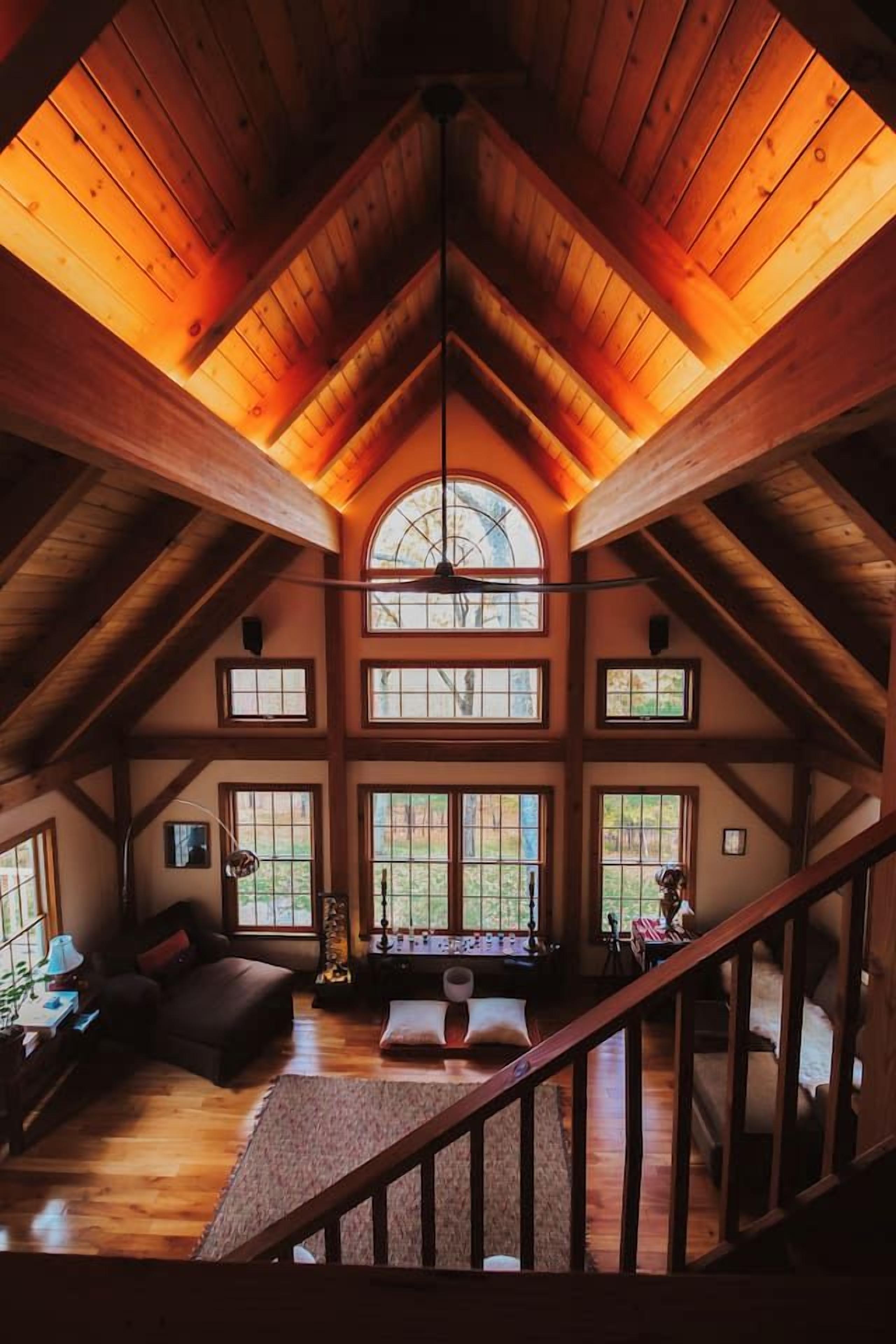 A spacious attic room with a high ceiling, wooden beams, and multiple windows.