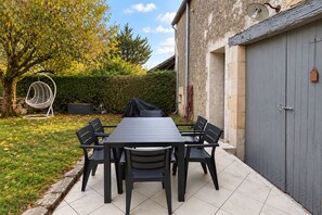 A rectangular outdoor dining table with six chairs, a hanging chair, and a covered grill, set against a stone wall and a hedge. - La Maison Talvanne – Character home with private pool (Donzy)