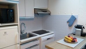 Una cucina con forno a microonde, lavello, fornello e una ciotola di frutta sul piano di lavoro.