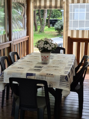 A covered outdoor dining area with a table set for four, surrounded by chairs, and a potted plant with flowers on the table. - Rental of a fully equipped 40-square-meter mobile home with a 20-square-meter covered patio (La Tremblade)