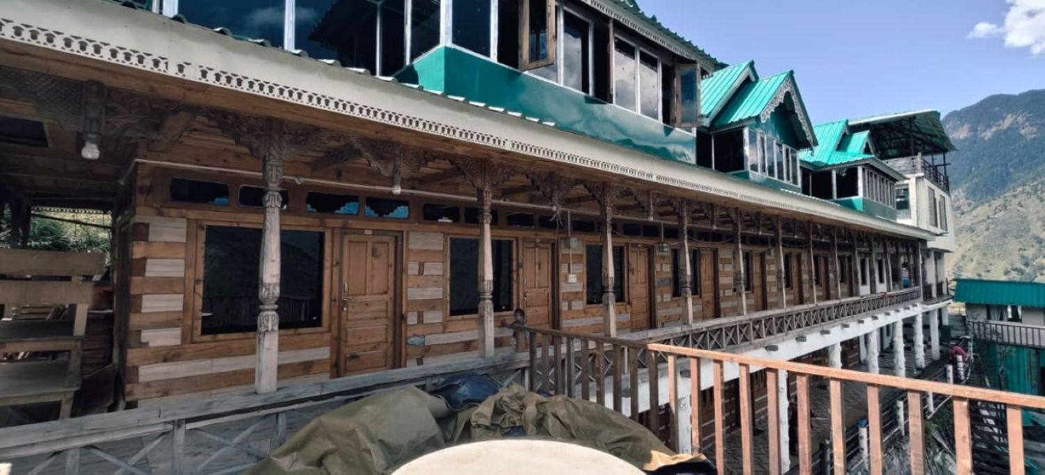 A traditional wooden building with a balcony, columns, and a mountainous backdrop.