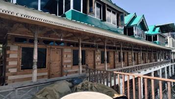 A traditional wooden building with a balcony, columns, and a mountainous backdrop.