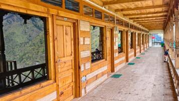 A wooden corridor with windows, a wooden floor, and a view of a mountainous landscape.