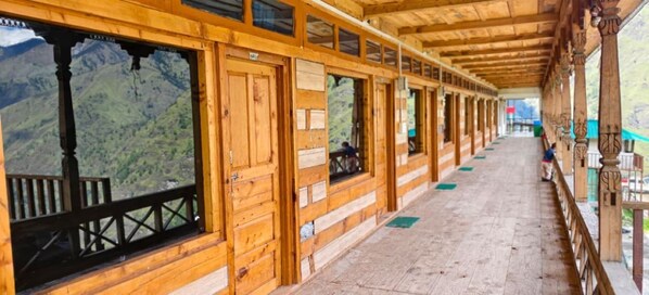 A wooden corridor with windows, a wooden floor, and a view of a mountainous landscape.