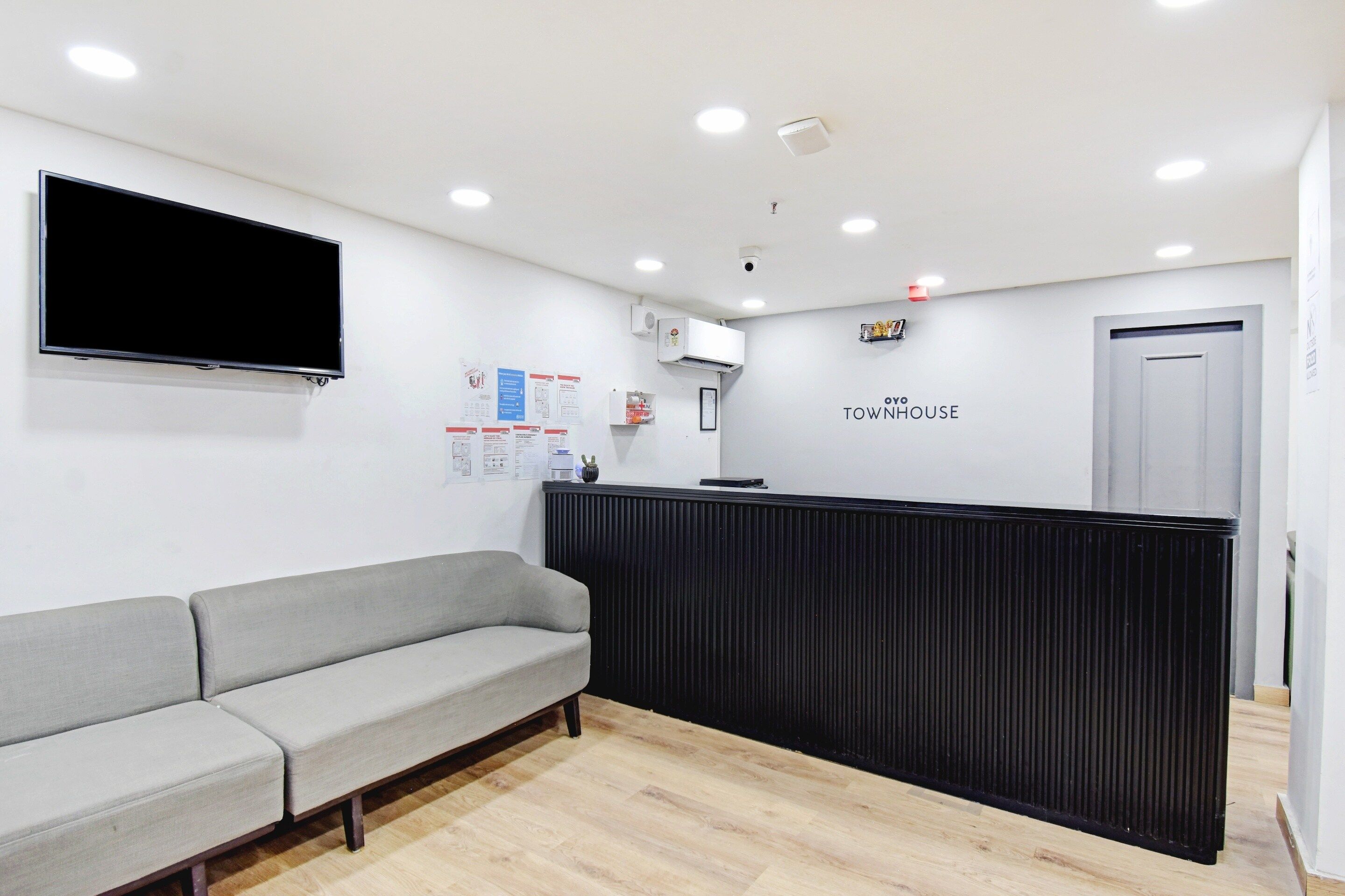 Zona de recepción con un sofá gris, un mostrador negro y un televisor de pantalla plana montado en la pared.