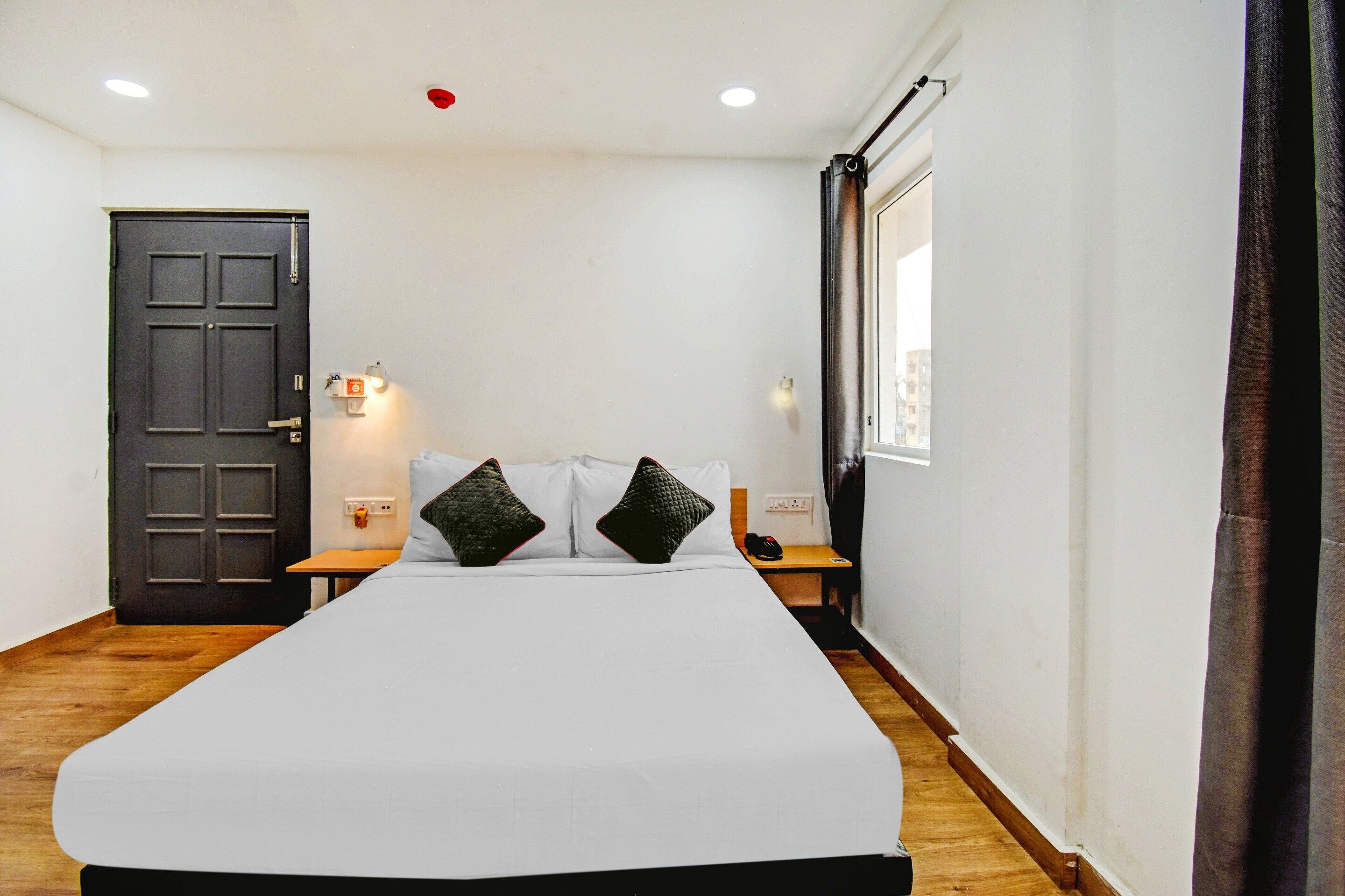 Ein Hotelzimmer mit einem großen Bett, einer Tür, einem Nachttisch, einer Wandleuchte und einem Fenster mit Vorhängen.
