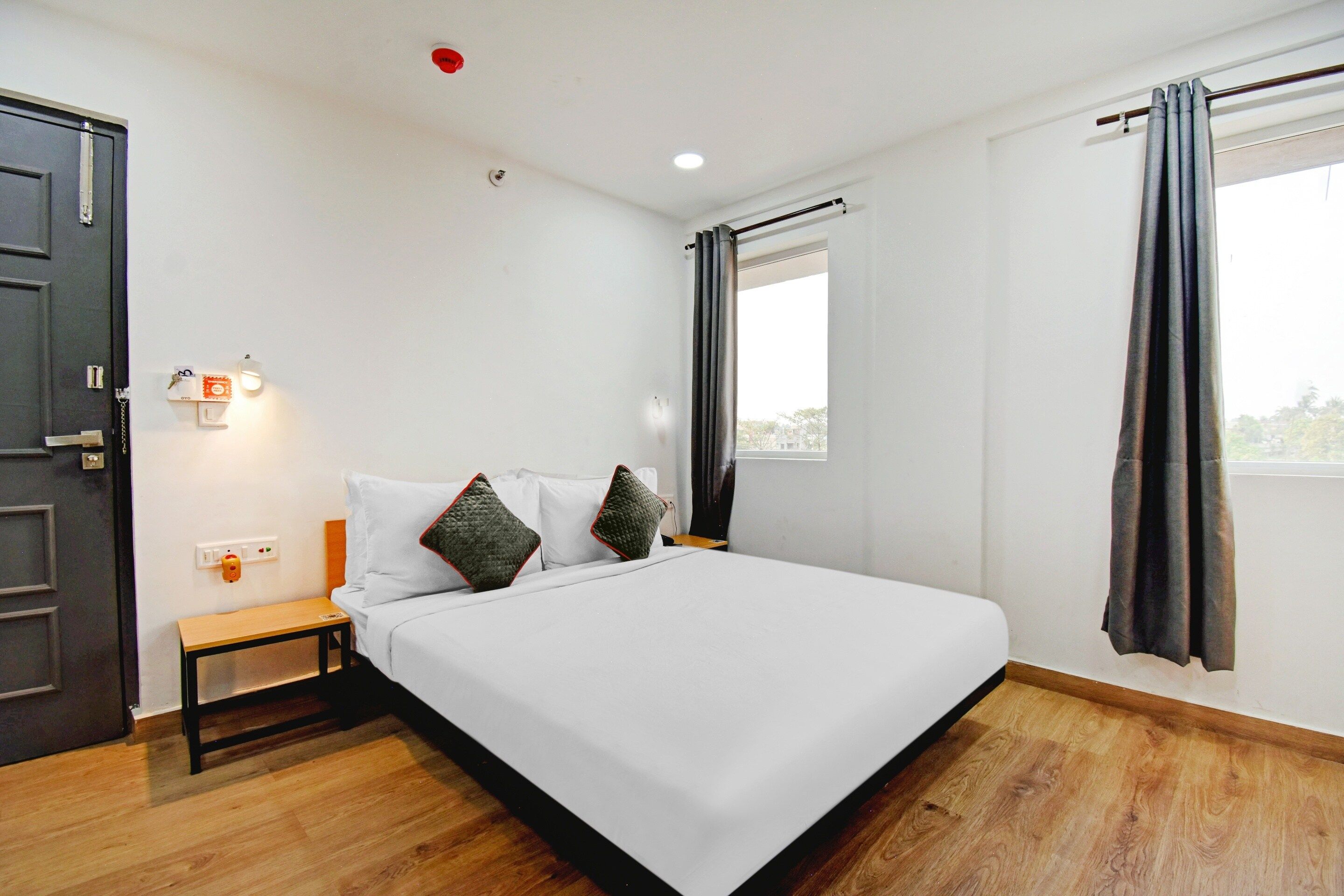 A hotel room with a bed, bedside table, and a window with curtains.