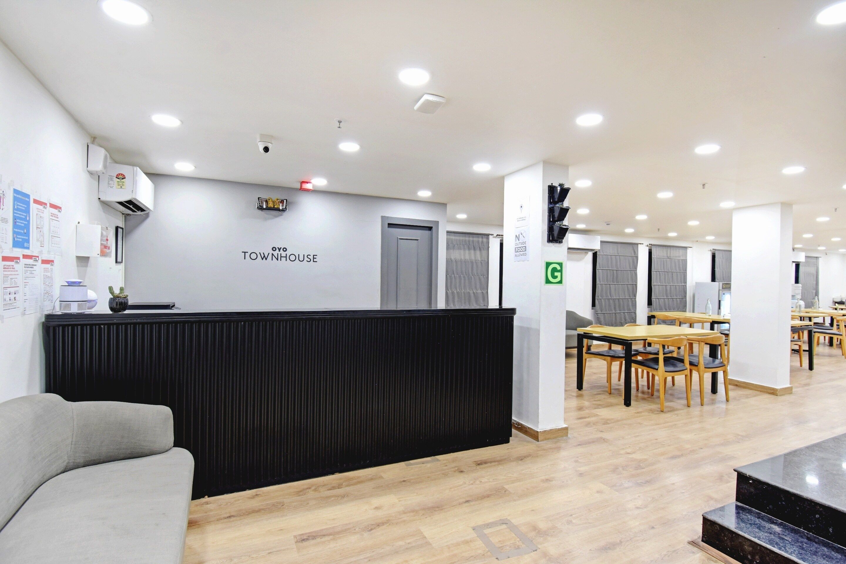 A modern office space with a reception desk, multiple tables and chairs, and a grey couch.