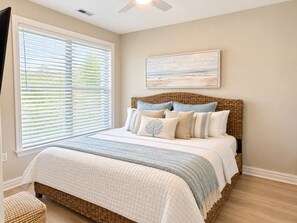 A bedroom with a bed, a ceiling fan, a window with blinds, and a painting on the wall. - Luxury Beach Condo | Pool | Surf | Swim | Arcade (Virginia Beach)