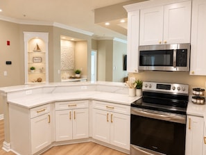 A kitchen with white cabinetry, a stainless steel oven, and a microwave. - Luxury Beach Condo | Pool | Surf | Swim | Arcade (Virginia Beach)