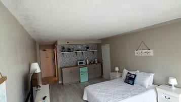 Une chambre à coucher comprenant un lit, des tables de chevet, un bureau avec une chaise, un four à micro-ondes et une armoire.