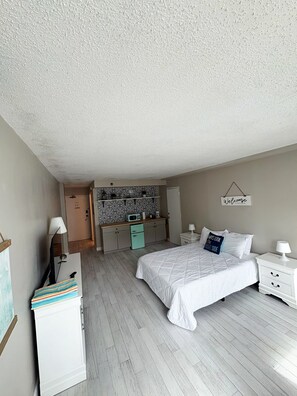 Een slaapkamer met een bed, nachtkastjes, een bureau met stoel, een magnetron en een garderobe.
