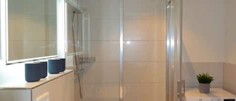 A modern bathroom with a glass shower enclosure, a sink with a faucet, and a front-loading washing machine.