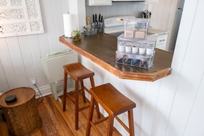Een keuken met een houten aanrecht, twee krukken, een kleine ronde tafel en een opbergmeubel met bakken.