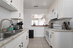 A kitchen with white cabinets, a stainless steel sink, a built-in oven, and a coffee maker. - High Tide · Upstairs 2BR · One Block to the Ocean (Jacksonville Beach)
