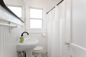 Een kleine badkamer met een wit wastafelmeubel, toilet en een raam boven de wastafel.