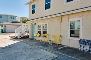 A two-story building with a garage, a staircase, and a row of yellow chairs outside. - Turning Tide · 1BR · No Stairs · Pet friendly (Jacksonville Beach)