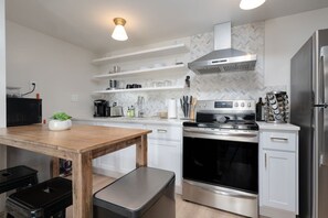 Une cuisine moderne avec des meubles blancs, une cuisinière en acier inoxydable et un four encastré. Deux suspensions sont fixées au-dessus du plan de travail.