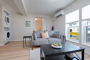 A modern living room with a grey sofa, a black coffee table, and a washing machine in the corner. - Turning Tide · 1BR · No Stairs · Pet friendly (Jacksonville Beach)