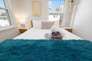 A neatly made bed with a fluffy blue rug, a bedside lamp, and a wall-mounted plant. - Rising Tide · Cozy 1BR Upstairs · Steps to Beach (Jacksonville Beach)