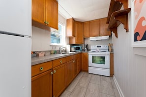 A kitchen with wooden cabinets, a white refrigerator, a microwave, and a stove. - Rising Tide · Cozy 1BR Upstairs · Steps to Beach (Jacksonville Beach)