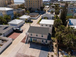 A multi-story residential building with a flat roof, a visible garage, and a small front yard with a palm tree. - Rising Tide · Cozy 1BR Upstairs · Steps to Beach (Jacksonville Beach)
