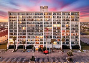 A multi-story hotel with a central courtyard, parking lot, and a view of the surrounding area. - The Allura- Galveston Condo Steps Away from Beach. Perfect for 4 people! (Galveston)