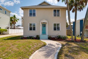 A two-story house with a front entrance, a pathway leading to the door, and a small garden area with palm trees. - Low Tide · 2BR/2BA · Private Deck · Steps to Sand (Jacksonville Beach)