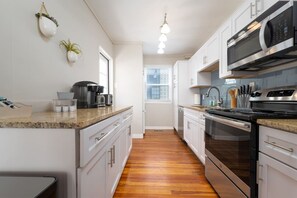 A modern kitchen with white cabinets, a granite countertop, stainless steel appliances, and a wooden floor. - Low Tide · 2BR/2BA · Private Deck · Steps to Sand (Jacksonville Beach)