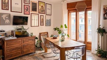 Un coin repas avec une table et des chaises en bois, un téléviseur, des œuvres d’art encadrées accrochées au mur et une vue sur l’extérieur par une fenêtre.
