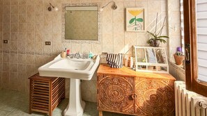 A bathroom with a pedestal sink, a wooden cabinet with intricate carvings, a mirror, and a framed artwork on the wall. - defaultName (Brienza)