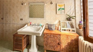 Une salle de bain avec un lavabo sur colonne, un meuble en bois orné de sculptures complexes, un miroir et une œuvre d’art encadrée accrochée au mur.