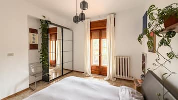 Une chambre à coucher avec un lit, un miroir, un radiateur, une fenêtre avec des rideaux et une plante.