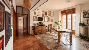 Un vaste espace dédié à la salle à manger, avec une table et des chaises en bois, un téléviseur fixé au mur et des œuvres d’art encadrées.