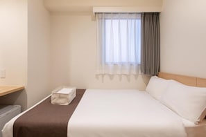Een hotelkamer met een bed, nachtkastje, raam met gordijnen en een stopcontact.