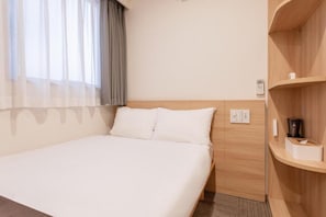 Een hotelkamer met een bed, nachtkastje, lamp en een raam met gordijnen.