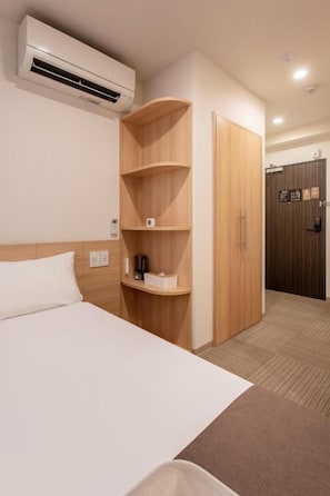 Een hotelkamer met een bed, een houten garderobe, een plankunit en een airconditioning.