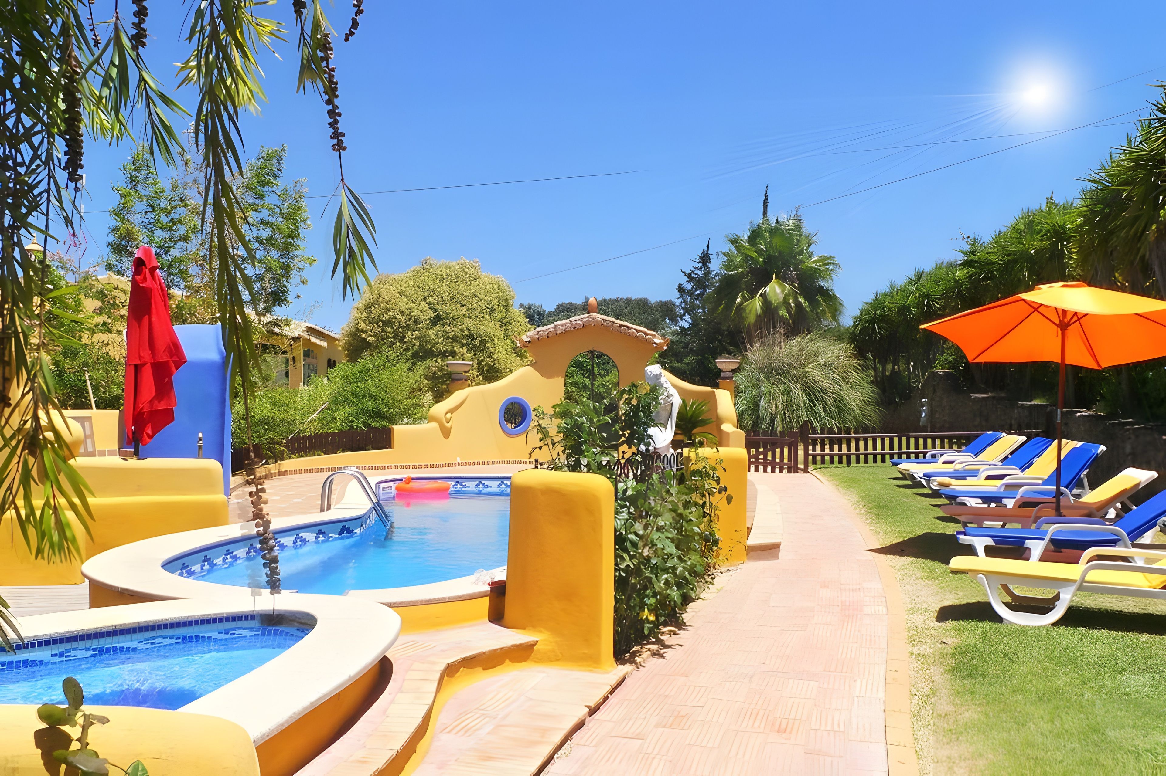 A pool area with multiple swimming pools, lounge chairs, and a red umbrella.