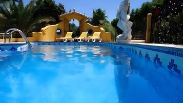Piscina con agua azul cristalina, rodeada de paredes amarillas y sillas de descanso blancas.