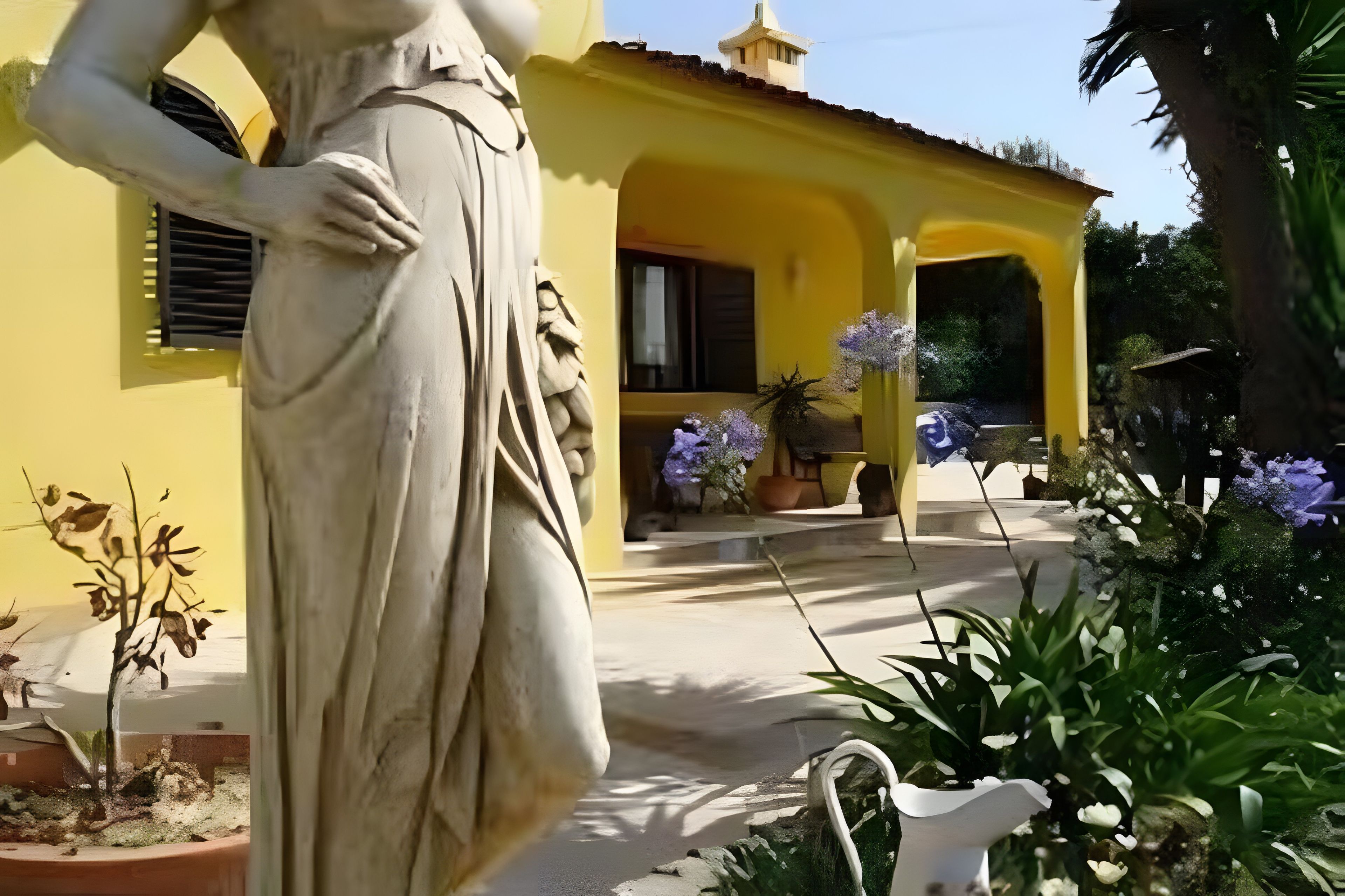 Una estatua de mujer en un jardín, con un edificio amarillo al fondo.
