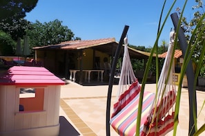 A patio area with a small wooden structure, a hammock, and a tiled floor.