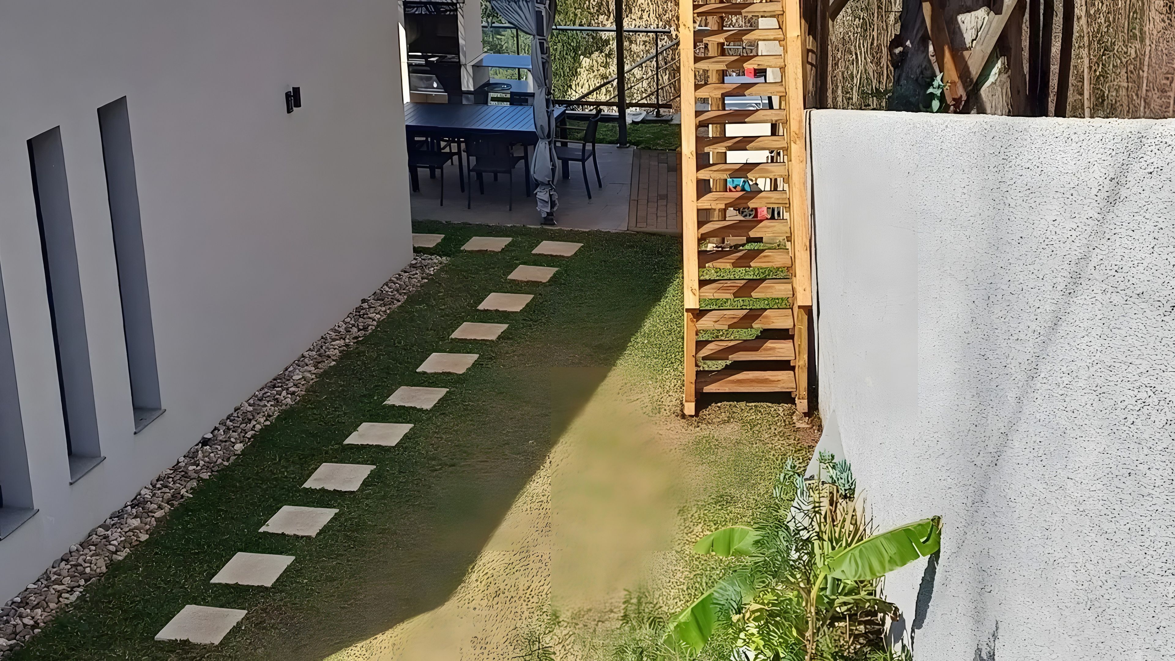 Un sentier étroit, parsemé de pierres plates, mène à un espace extérieur aménagé avec une table et des chaises.