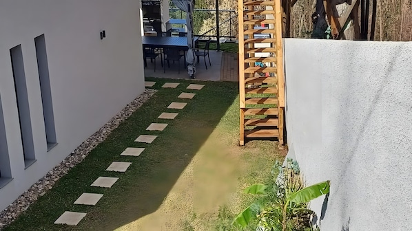 Un sentier étroit, parsemé de pierres plates, mène à un espace extérieur aménagé avec une table et des chaises.