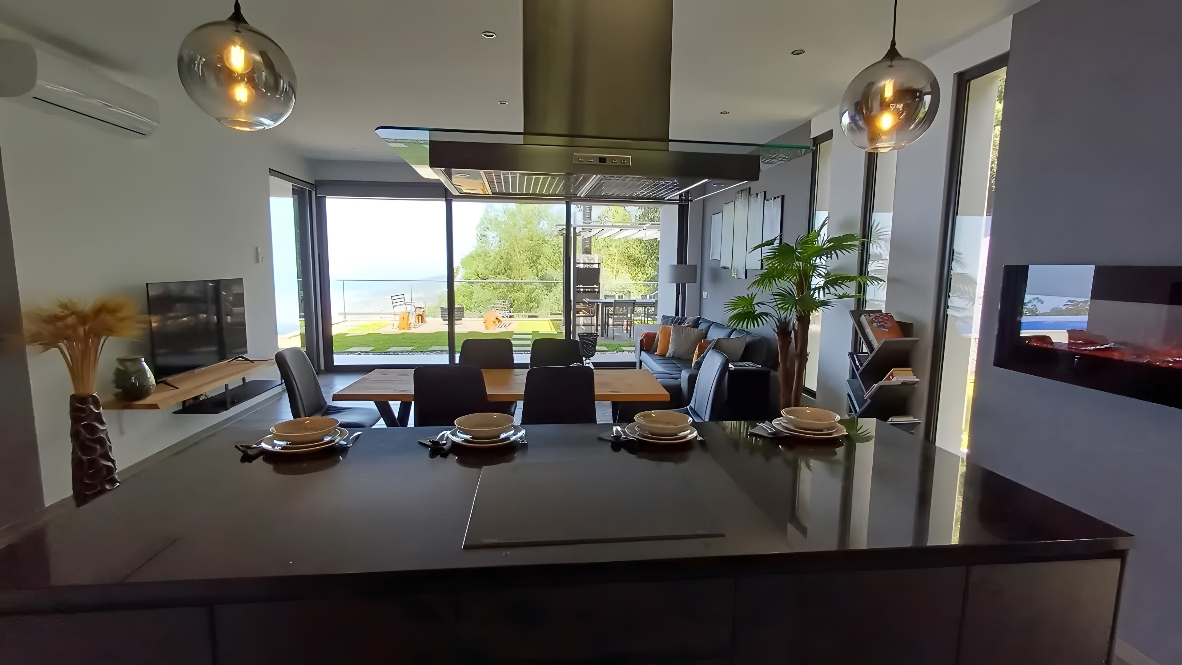 Eine moderne Küche mit einer zentralen Kochinsel, Essbereich und großen Fenstern mit Blick ins Freie.