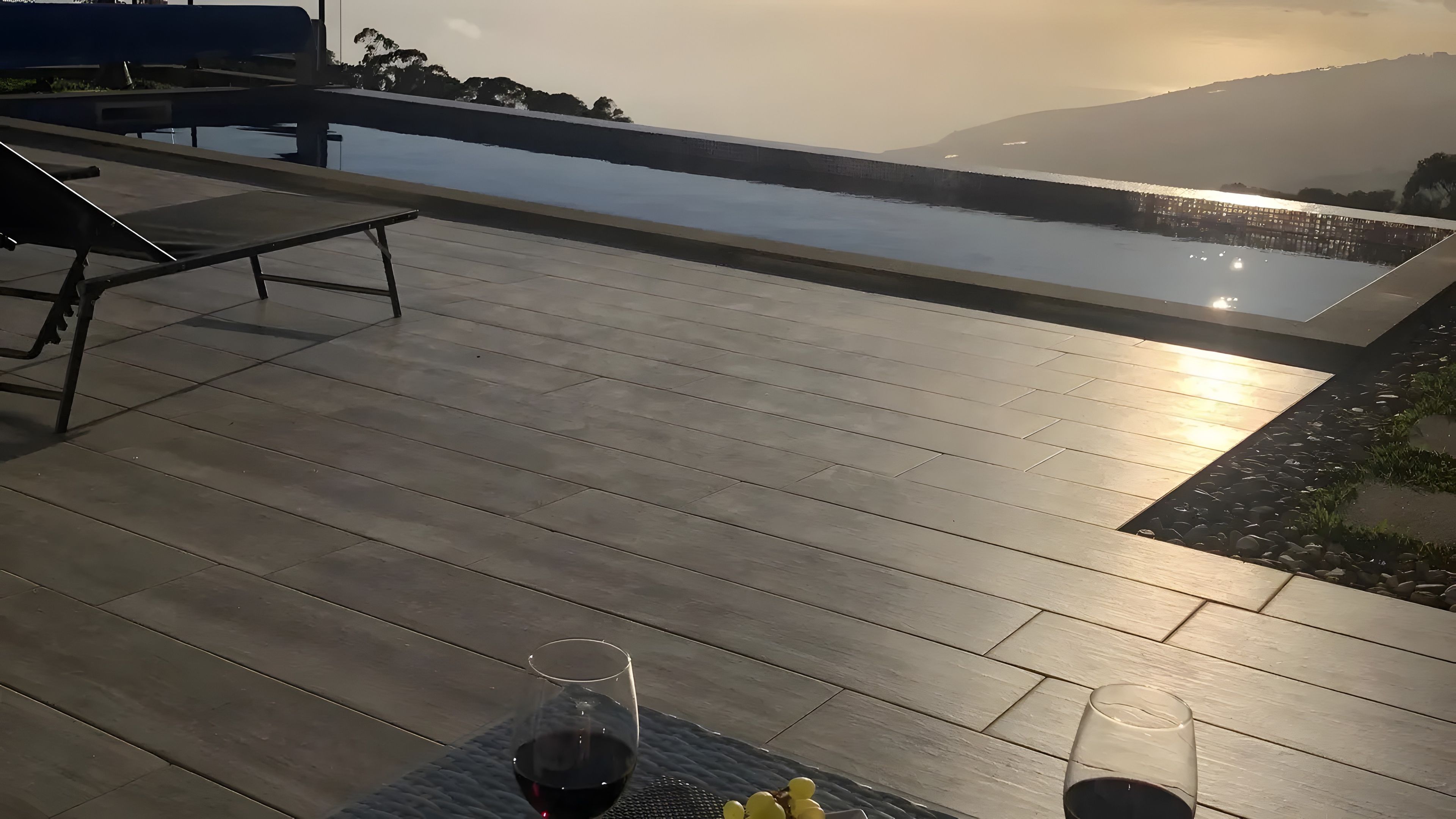 Une terrasse en bois avec une piscine, des chaises longues et un verre de vin rouge.